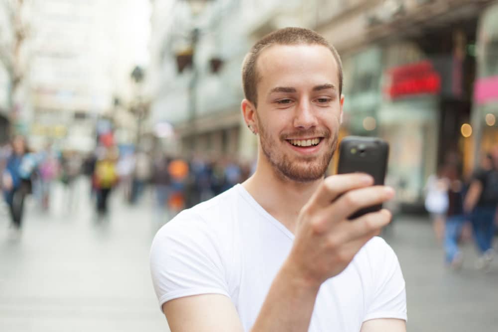 Image of young man wearing a white t-shirt, checking email or notification on his mobile phone - Juan Rojo Design