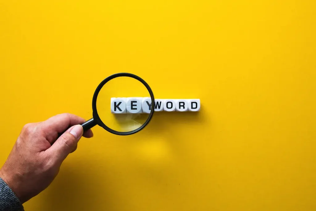 How to Find Seed Keywords for Free | Concept image of a male hand holding a magnifying glass to a series of blocks spelling out the word keyword - Juan Rojo Design Toronto